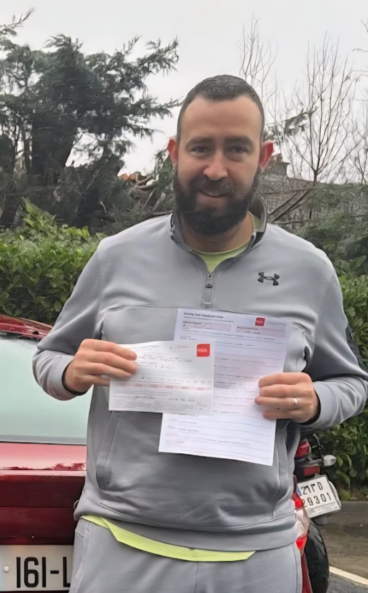 Student holding his driving test pass certificate beside his car