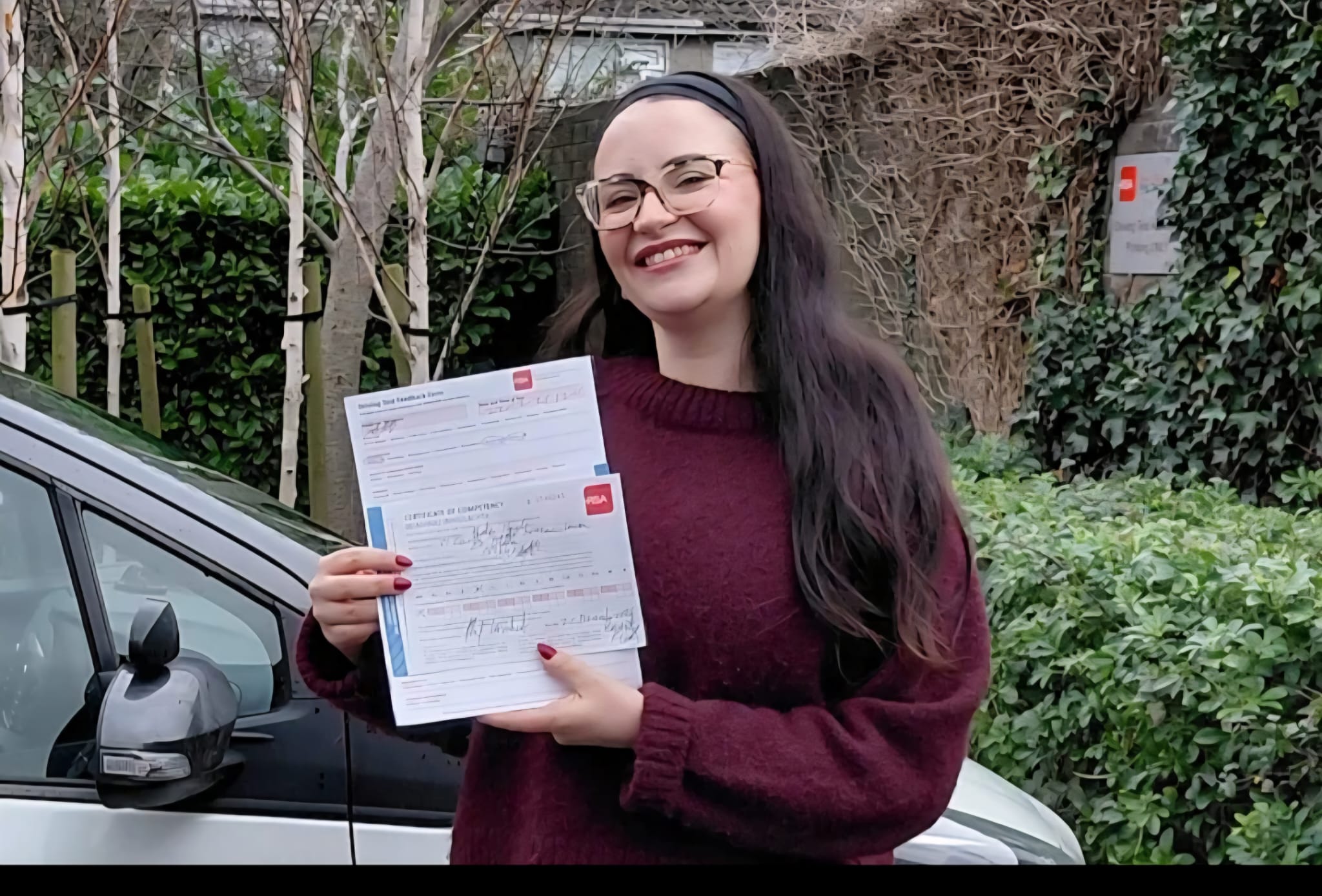 Smiling student with her pass certificate in front of the car
